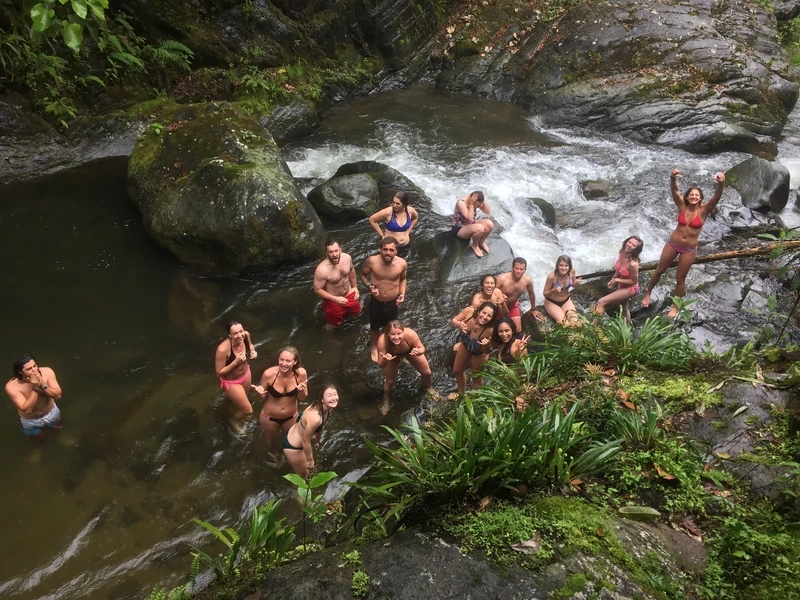Volunteers swimming and posing in a jungle river pool below a waterfall