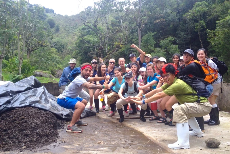 Volunteers posing together at a work site beside a compost pile in the Costa Rican highlands
