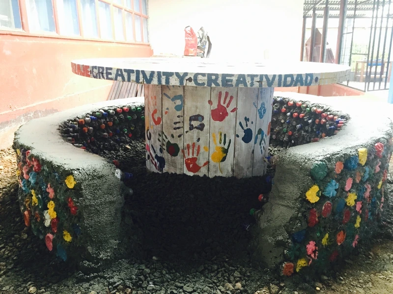 A finished community bench and table built from concrete and recycled bottle caps, painted with handprints and the word Creativity