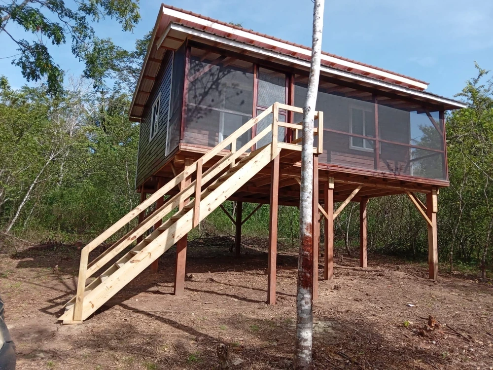 The finished cabin raised on posts, with a red roof and new pale timber stairs