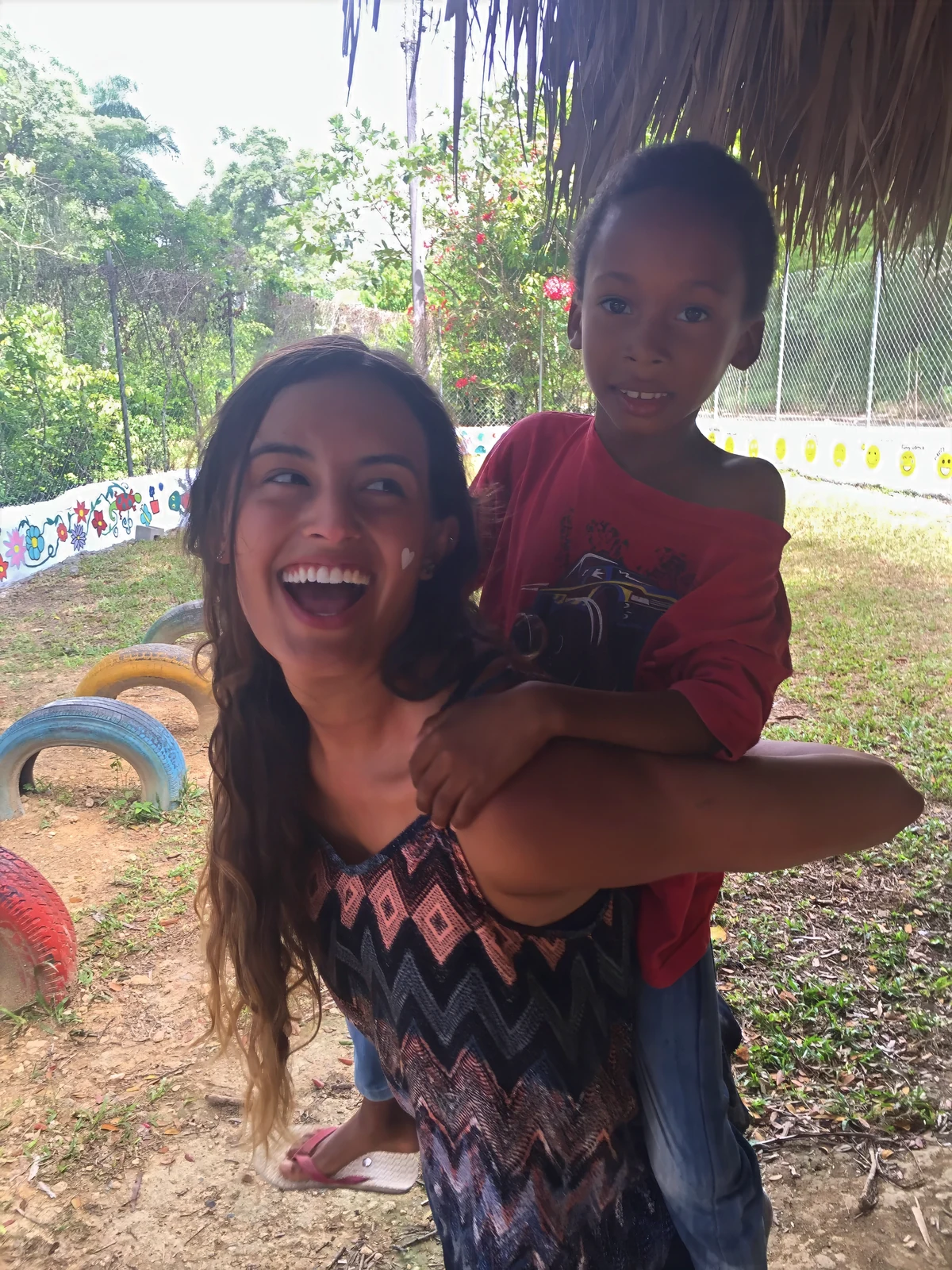Community development volunteer abroad giving a young child a piggyback ride on a playground
