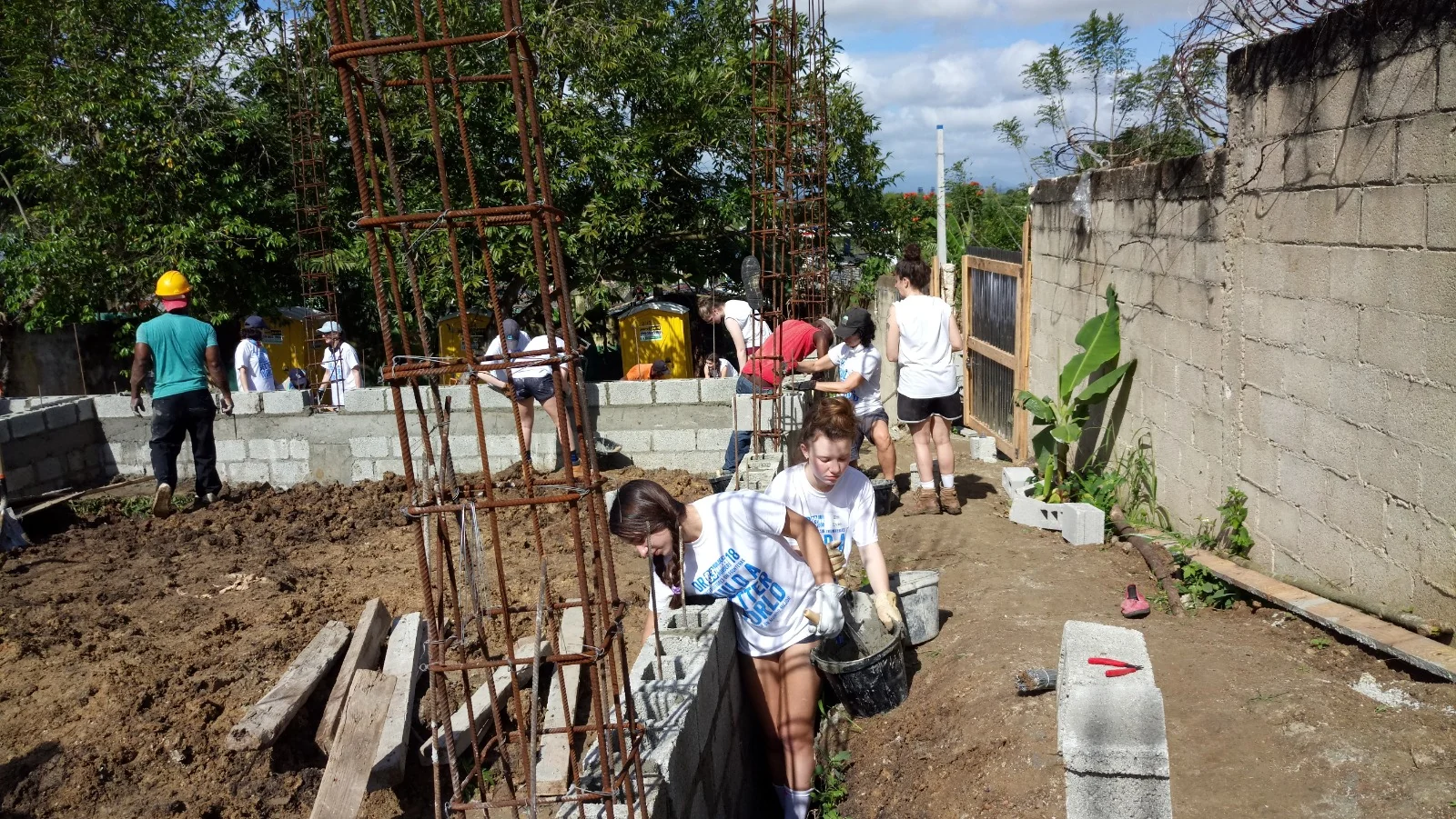 Volunteers and local builders laying concrete block and setting rebar on a community construction site